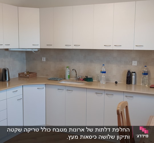 מטבח עם ארונות לבנים, מקרר, קומקום אדום, כיור וברז